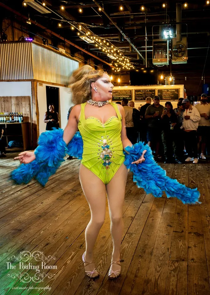 A drag performer in a lime bodysuit and blue feather boa working the room at Dirty Tea