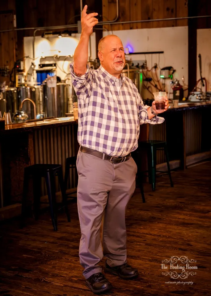 A guest dancing with one arm raised beside the distillery tanks