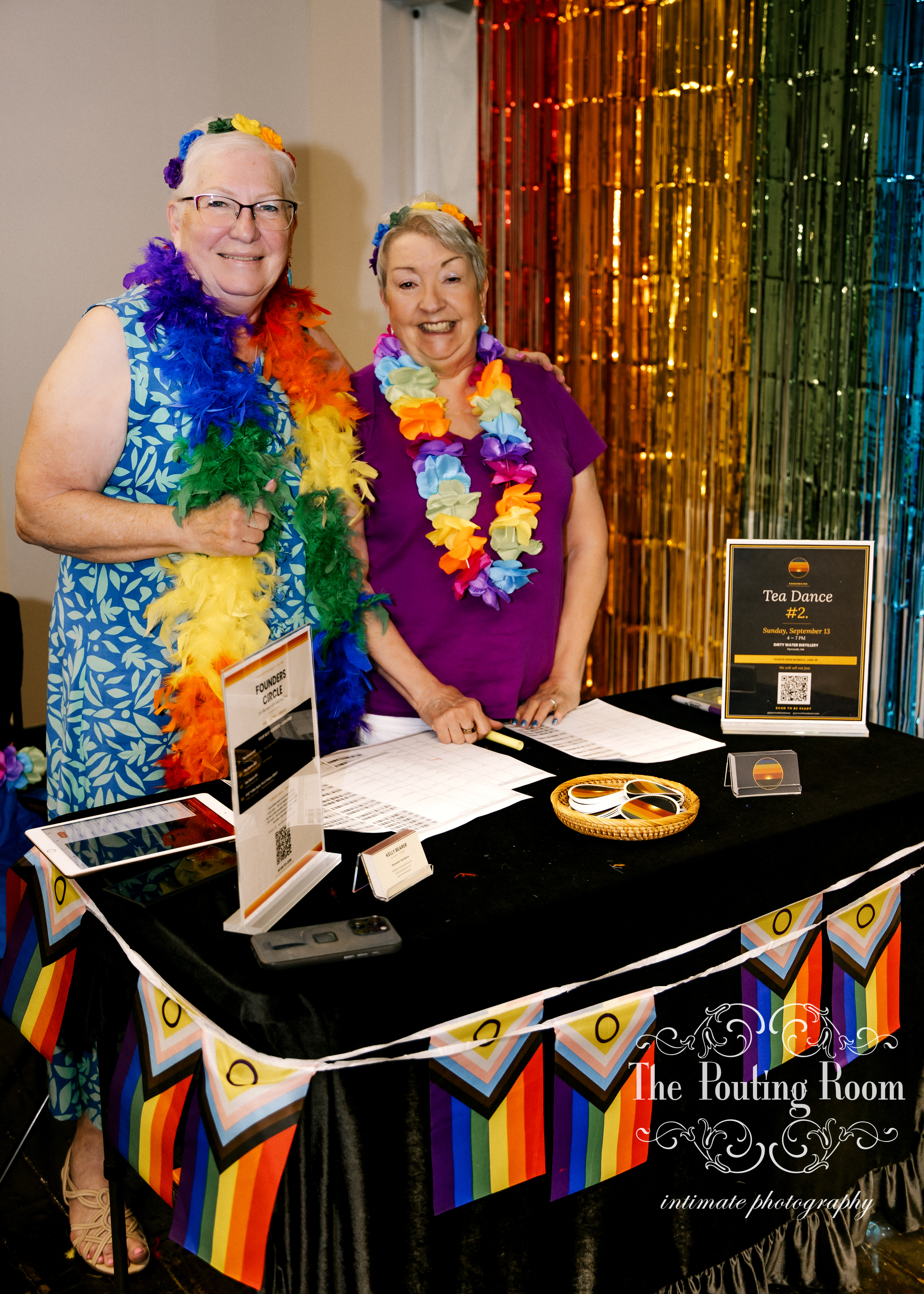 Two guests at the welcome table beneath Progress Pride bunting at the Inaugural Tea Dance